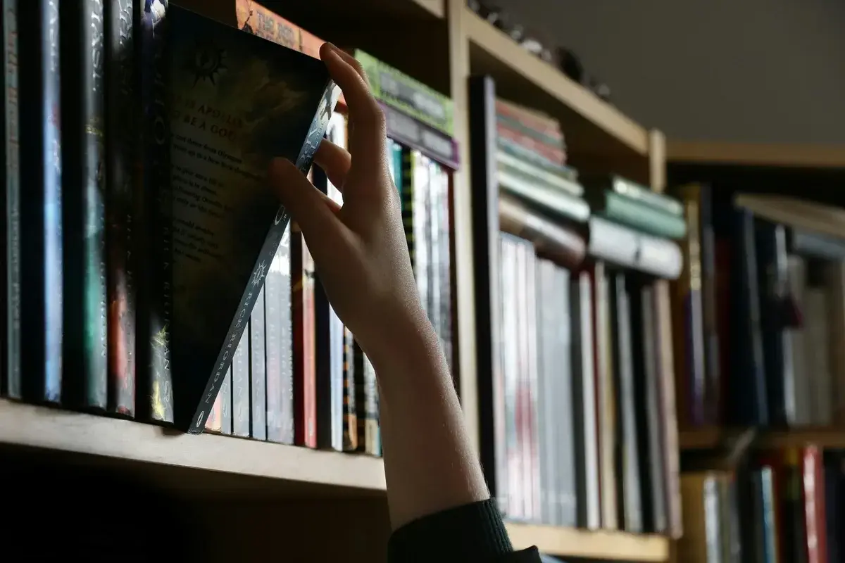 Una mano sfila un libro da uno scaffale di una biblioteca.