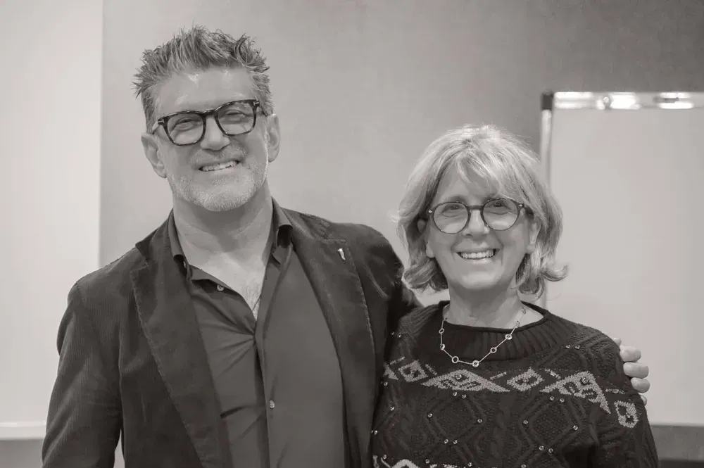 Due persone sorridenti in un ambiente professionale, con un muro e una lavagna alle spalle. Ernesto Bruschi e Nadia Martina.
