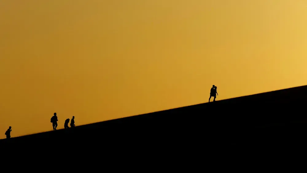 Silhouettes of people walking up a hill against a sunset backdrop.
